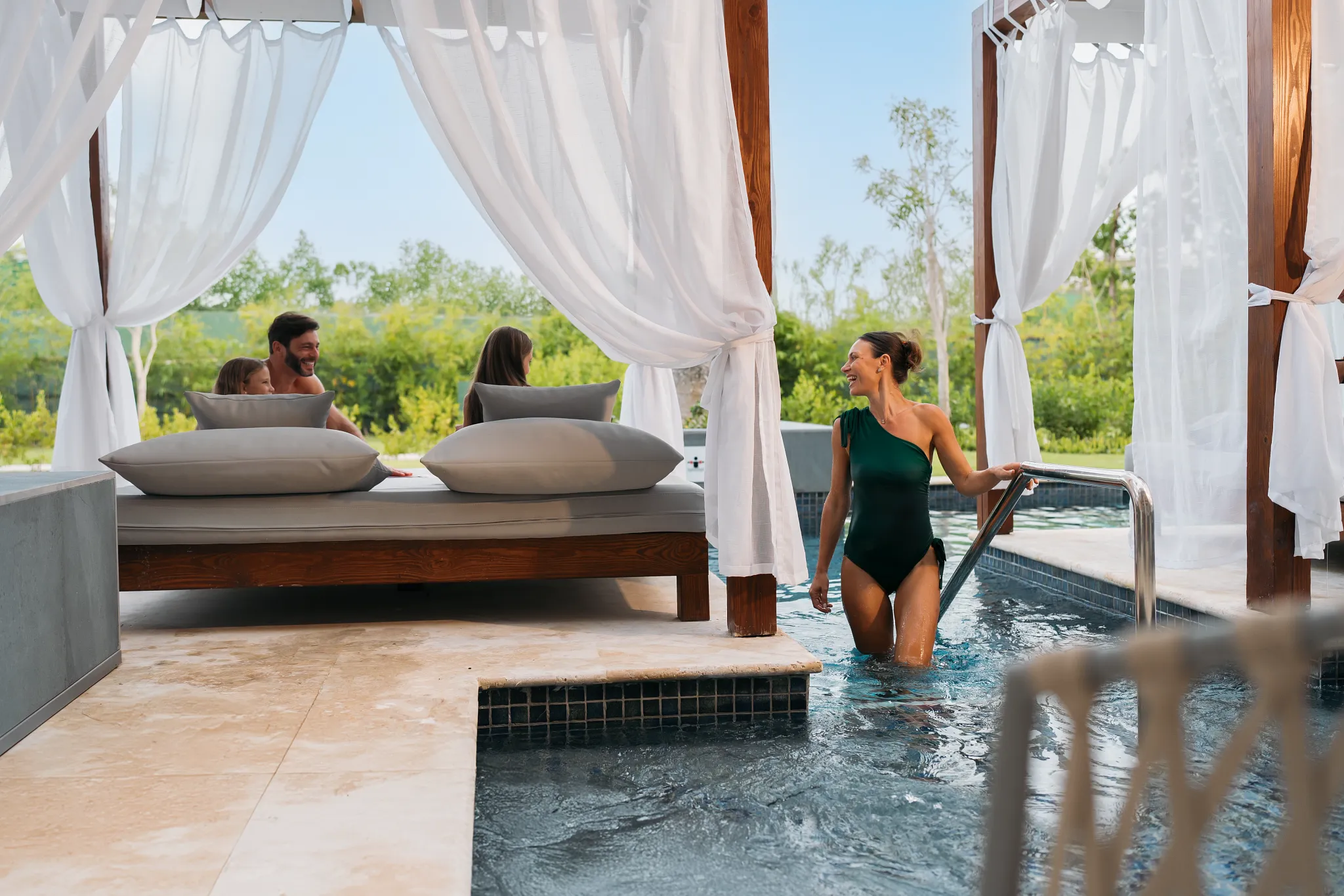 Family enjoying refreshing drinks on a poolside Bali bed at Dreams Royal Beach Punta Cana with attentive service.