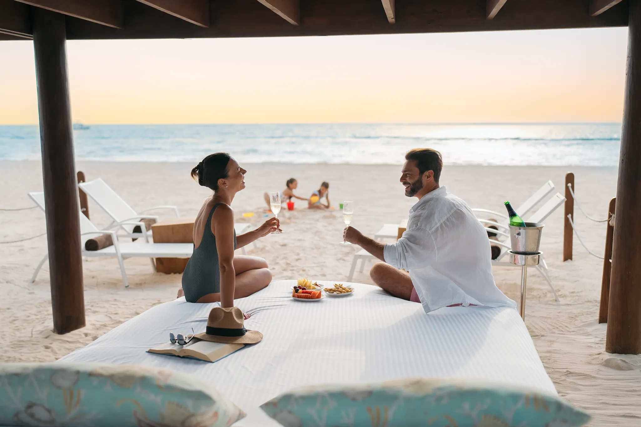 Couple enjoying champagne on a private beach setup at Dreams Royal Beach Punta Cana while children play nearby.