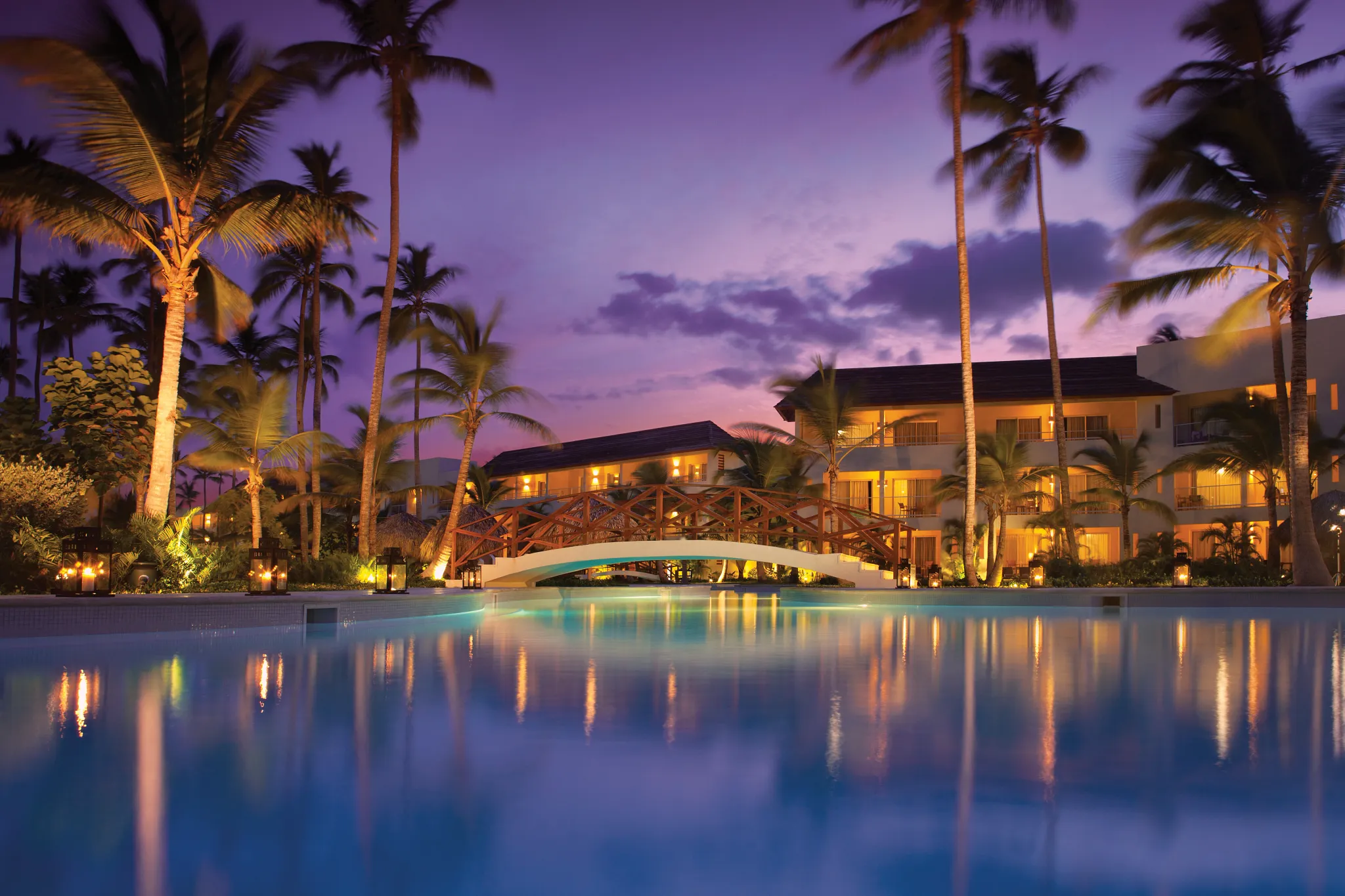 Illuminated pool with bridge and palm trees at sunset at Dreams Royal Beach Punta Cana.