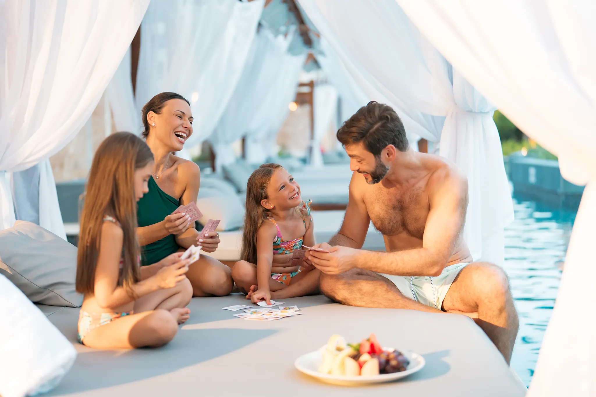 Family playing cards and enjoying snacks on a Bali bed at Dreams Royal Beach Punta Cana in a private cabana setting.