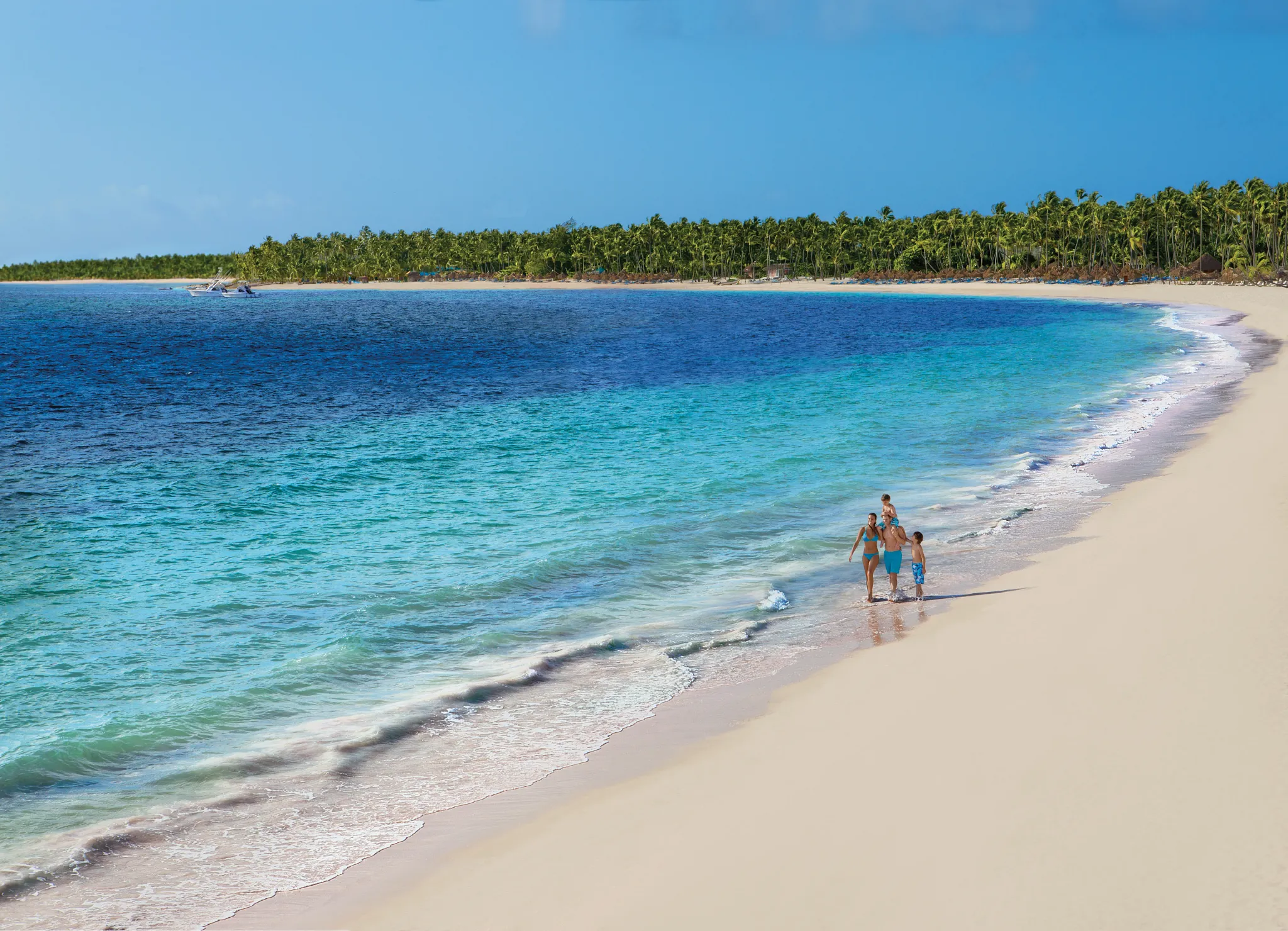 Family walking along a pristine white-sand beach with turquoise water at Dreams Royal Beach Punta Cana.