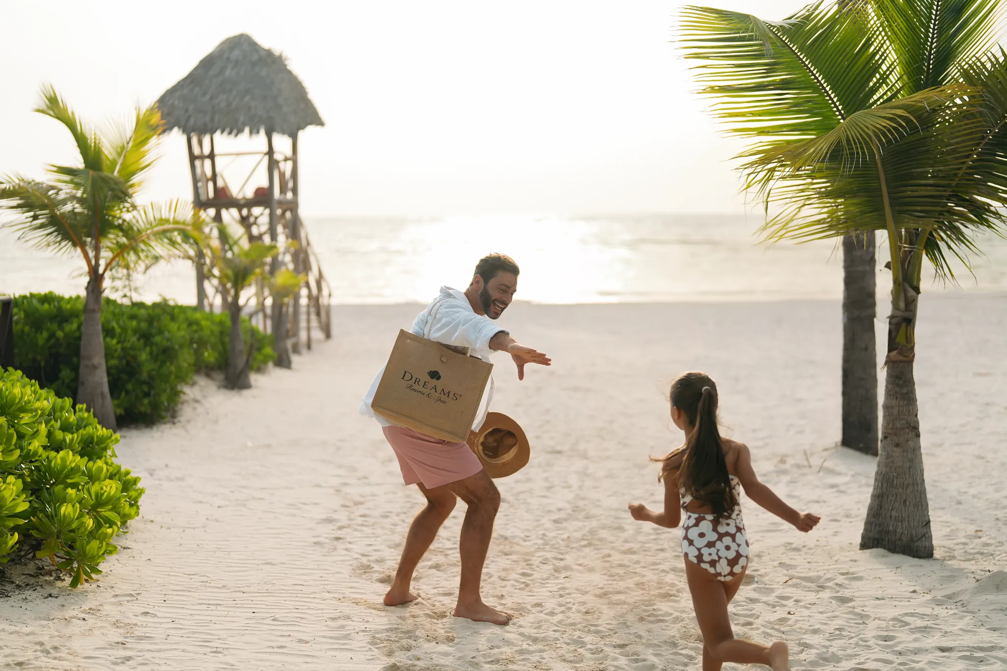 Father and daughter playing together on a sandy beach at Dreams Royal Beach Punta Cana during sunset.