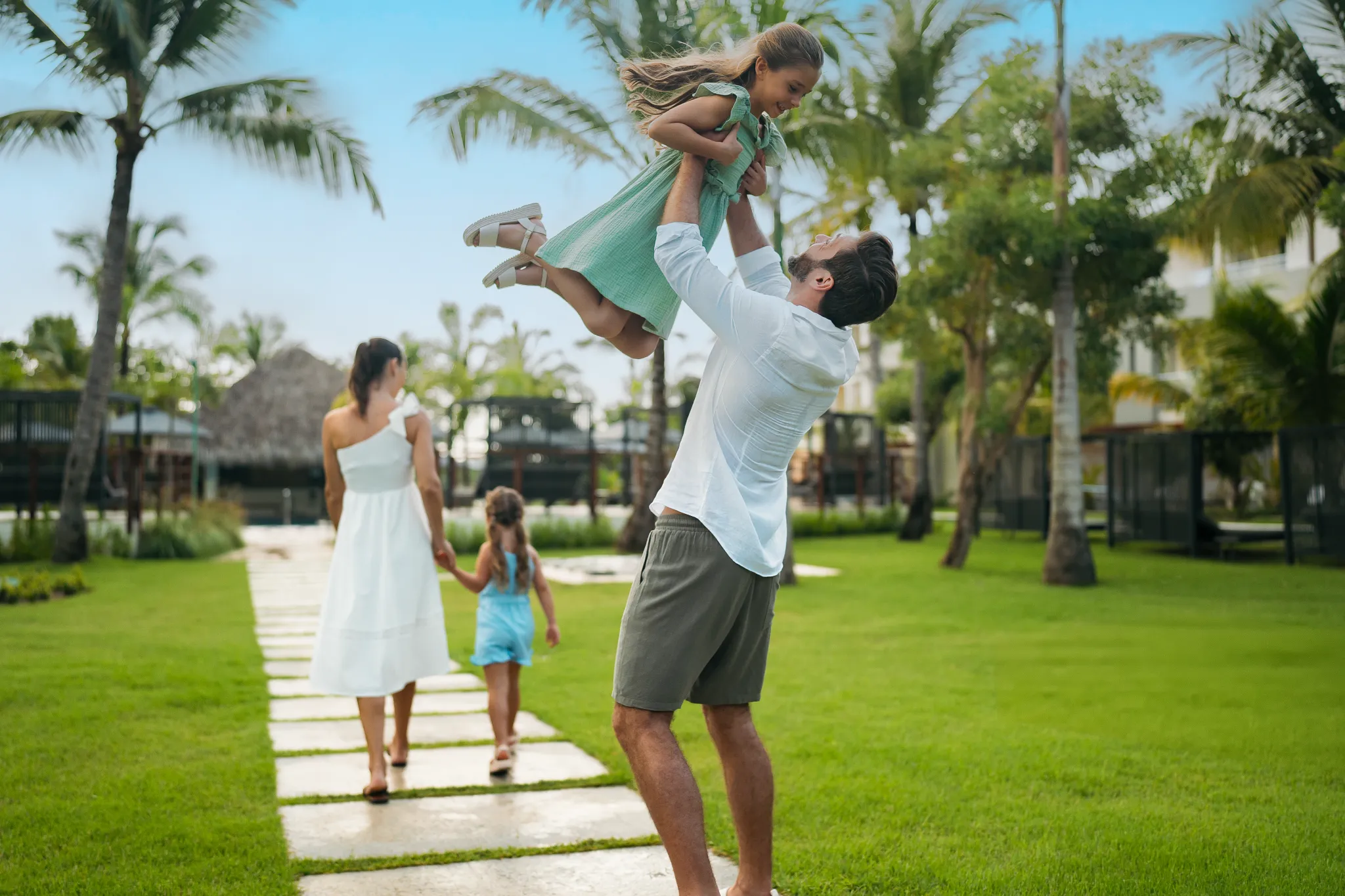 Father lifting daughter while family walks through tropical gardens at Dreams Royal Beach Punta Cana, highlighting family-friendly resort grounds.