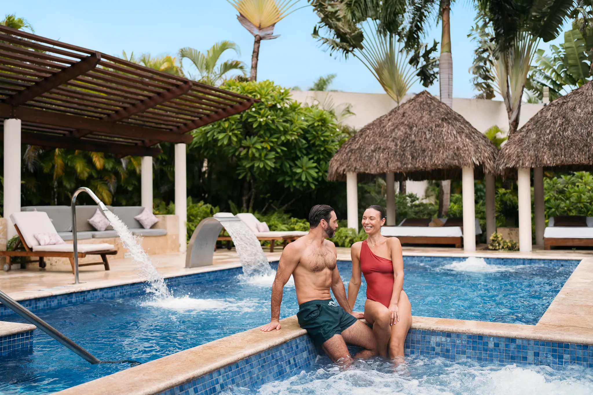 Couple relaxing in hydrotherapy pool at Dreams Royal Beach Punta Cana spa with waterfalls and loungers.