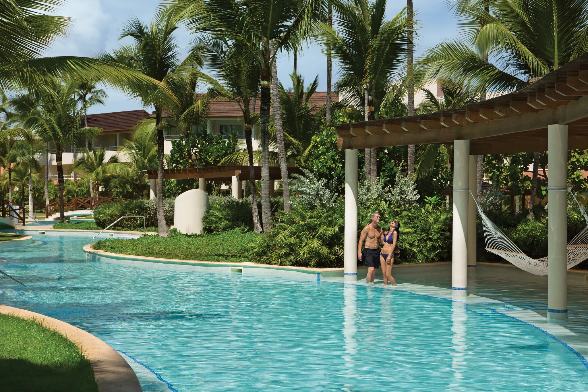 Couple walking through a lazy river-style pool surrounded by lush gardens at Dreams Royal Beach Punta Cana.