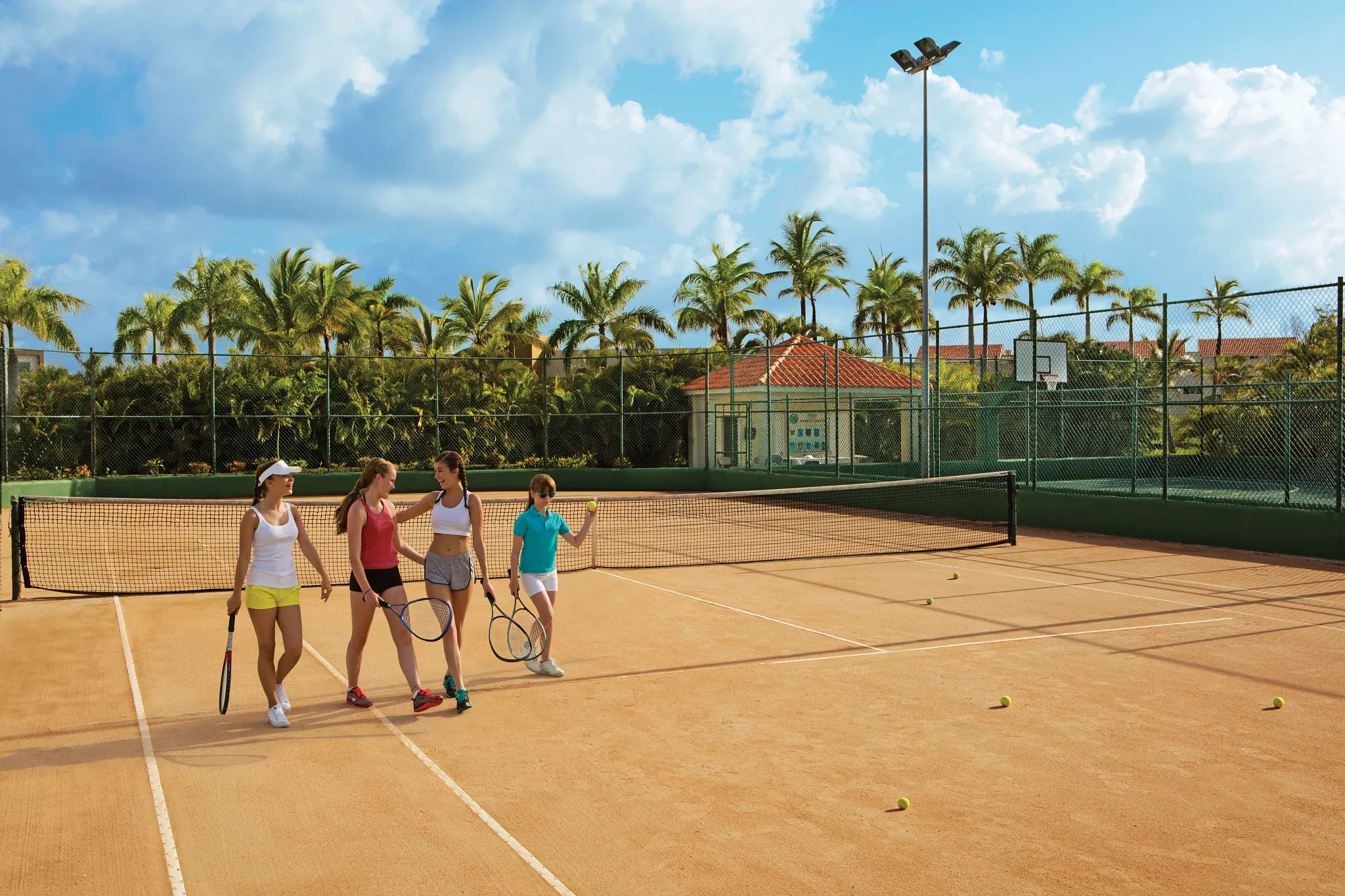 Guests playing tennis on outdoor courts surrounded by palm trees at Dreams Royal Beach Punta Cana.